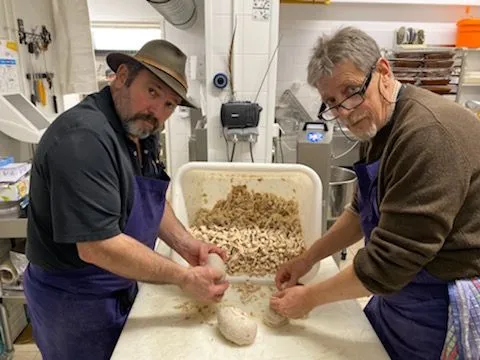 Deux hommes en train de pétrir de la pâte dans une cuisine.